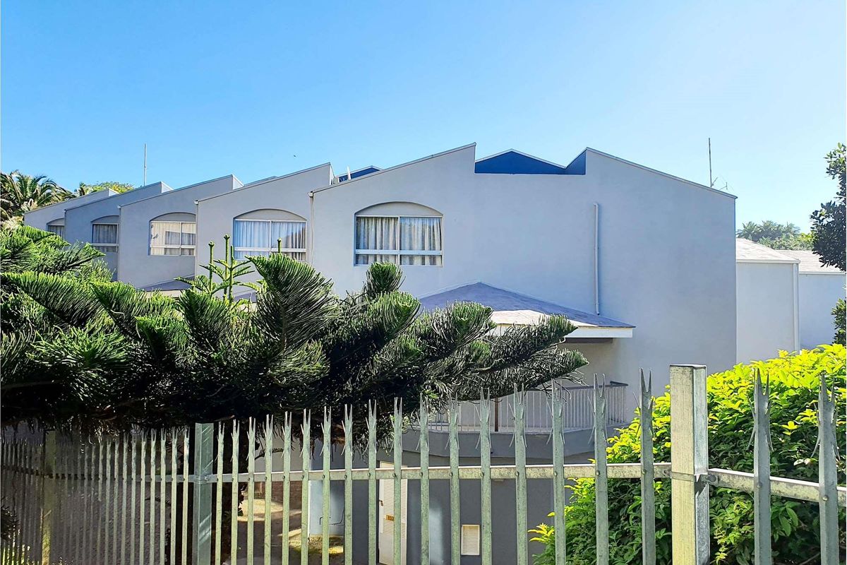 Rear view of a multi-unit commercial building featuring a pitched roof design, balcony with metal railing, and secure perimeter fencing.