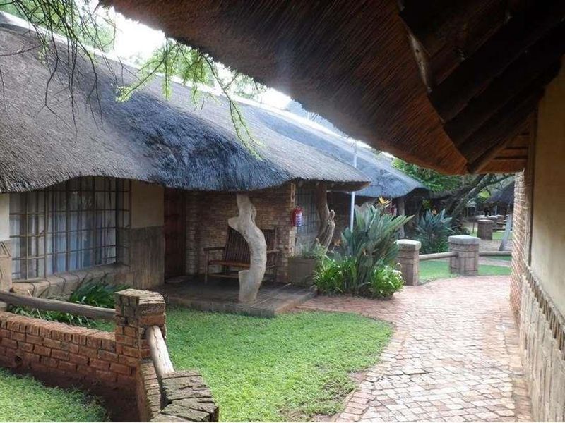 A view of the lodge exterior featuring traditional thatch roofing, brick construction, and a paved walkway leading past the units.