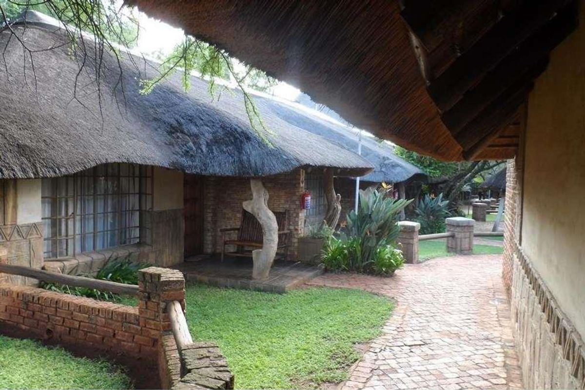 A view of the lodge exterior featuring traditional thatch roofing, brick construction, and a paved walkway leading past the units.