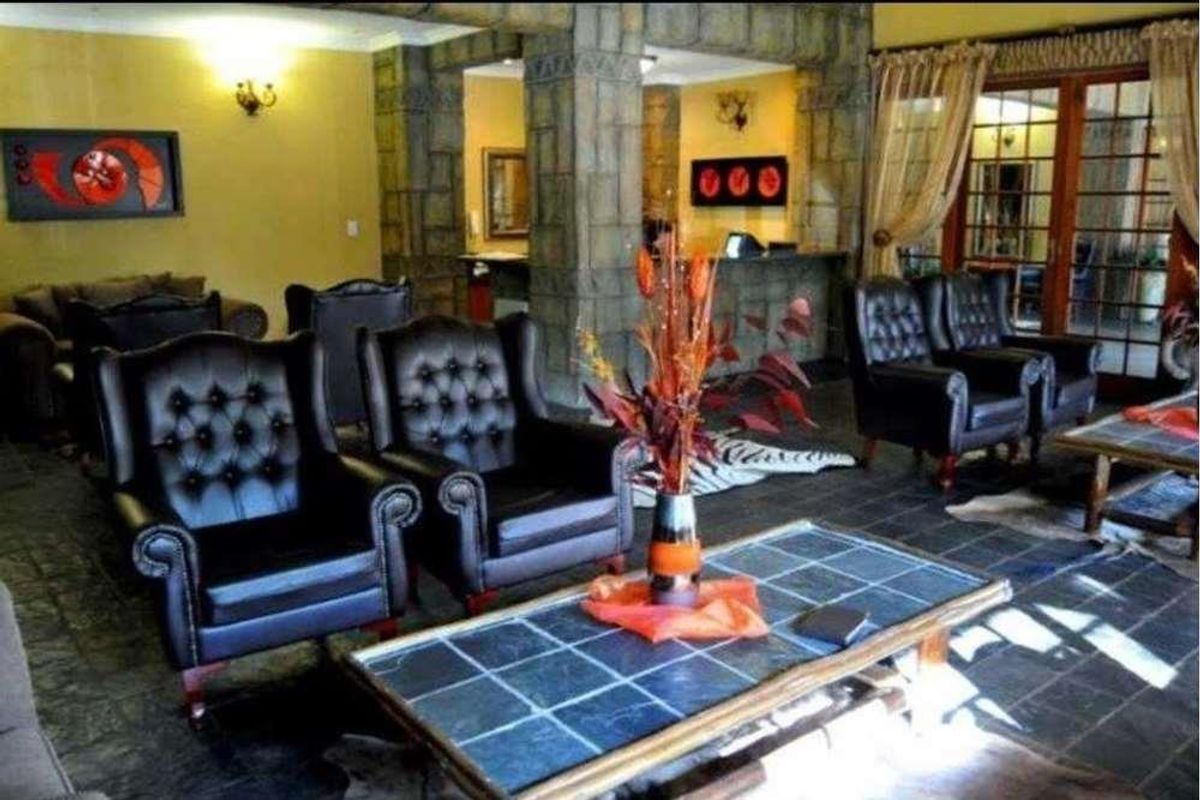 Spacious lodge living area featuring rustic stone-clad pillars, dark slate tile flooring, and large wooden-framed glass doors leading to the exterior.
