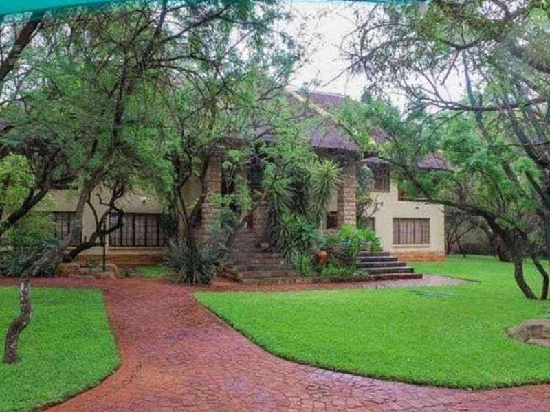 A charming lodge-style property featuring a stone facade, thatched roof, and a well-maintained garden with a paved entrance path.
