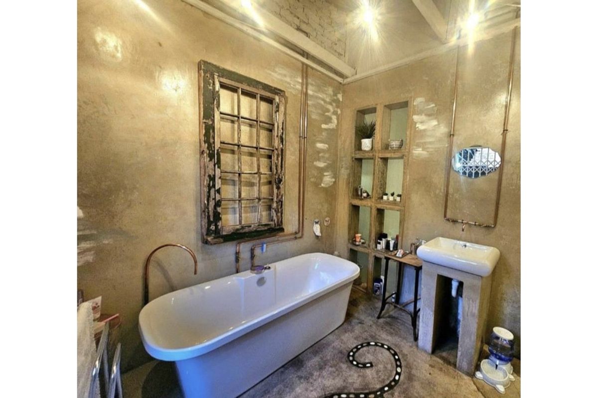 A rustic-style bathroom featuring a freestanding bathtub, pedestal sink, and exposed copper plumbing with built-in wall shelving.