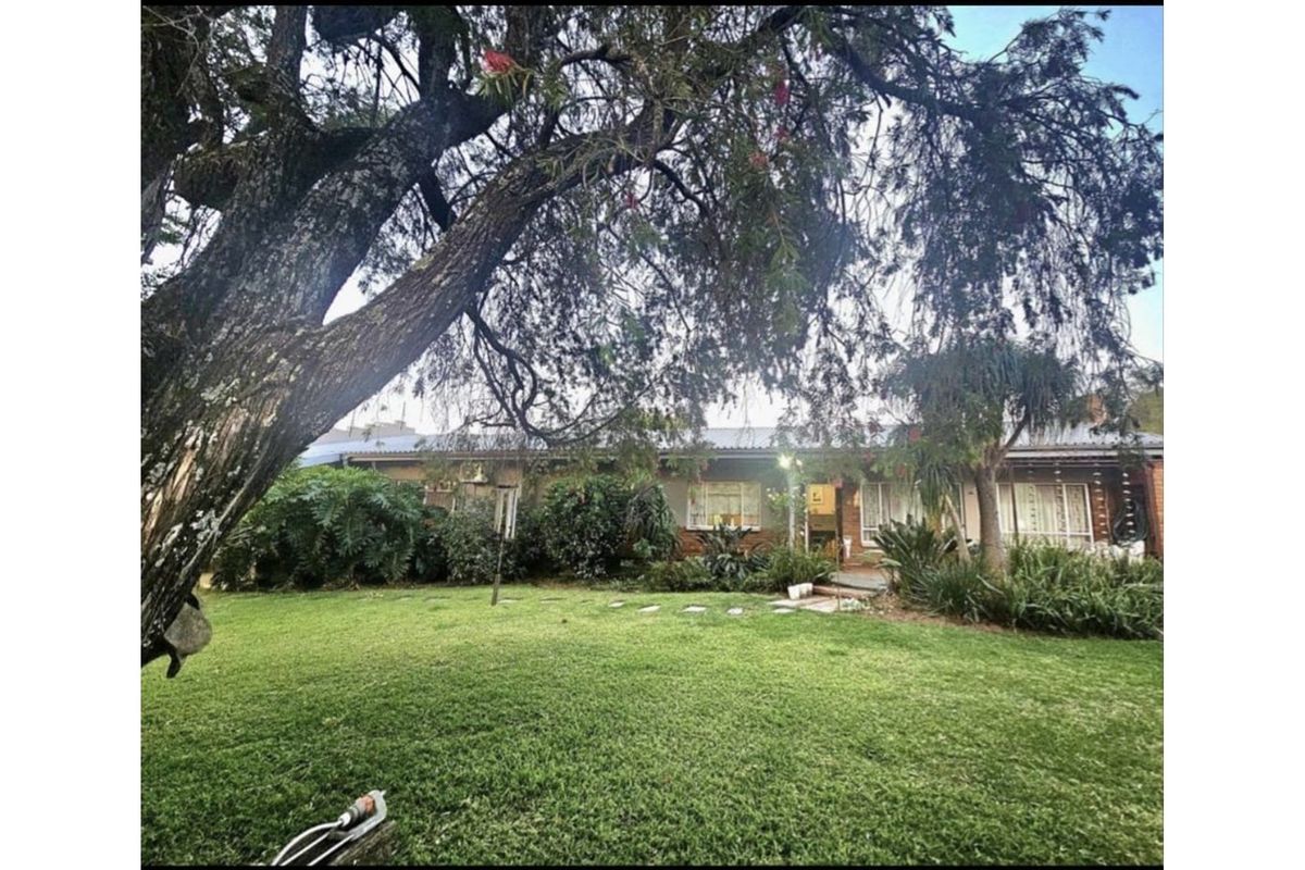 A view of the rear exterior of the house featuring a large garden, mature trees, and established landscaping.