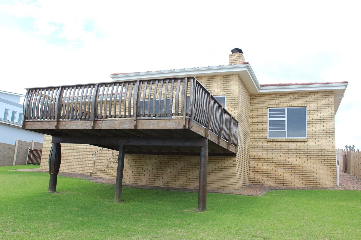 Rear view of the property featuring a raised timber deck with balustrades, brick facade, and a chimney stack overlooking the garden.