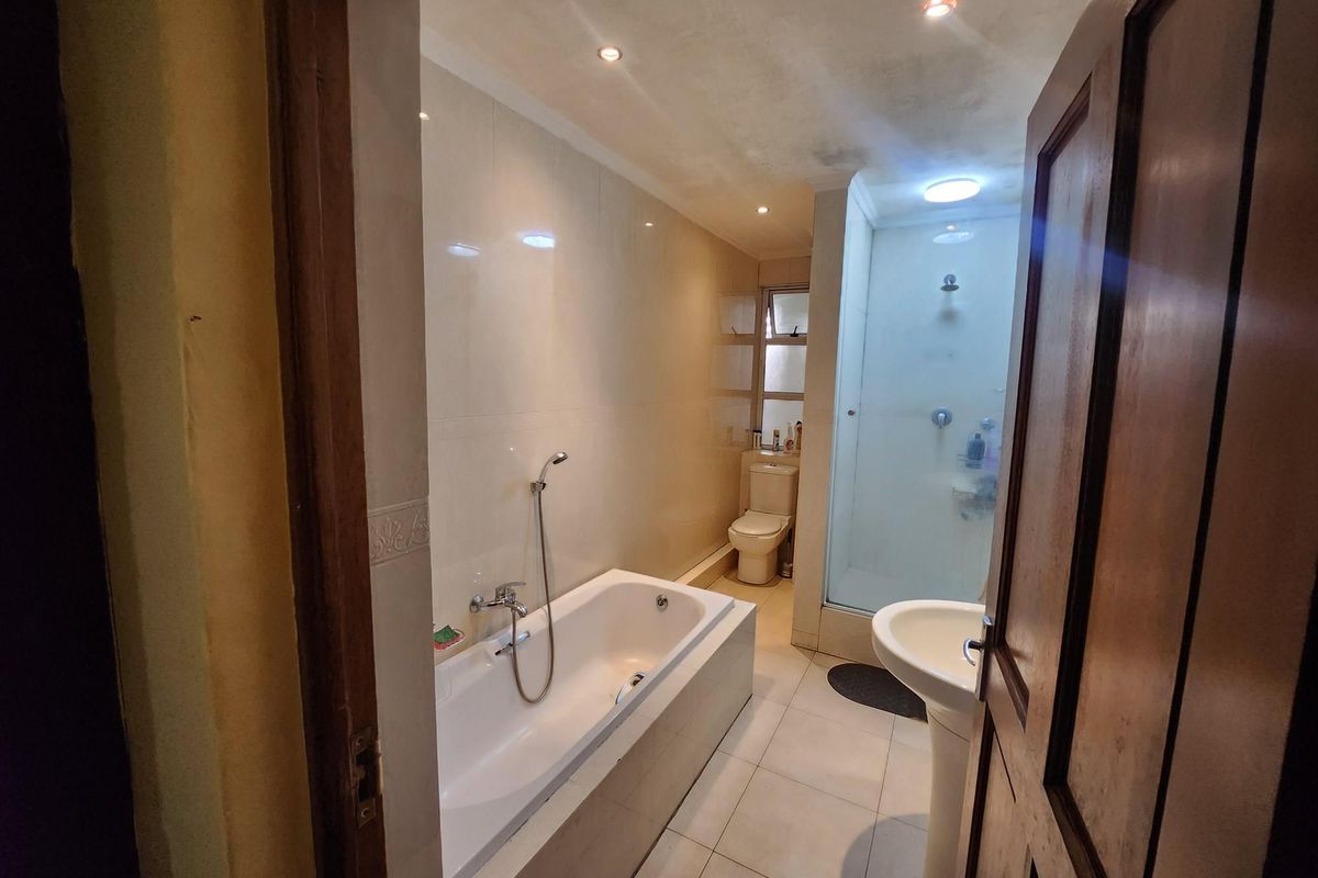 A functional bathroom featuring a built-in bathtub, separate glass-enclosed shower, pedestal basin, and toilet with tiled walls and flooring.