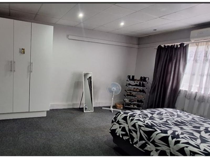 Spacious bedroom featuring built-in wardrobes, carpeted flooring, and a wall-mounted air conditioning unit.