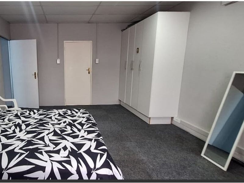 A bedroom featuring grey carpeted flooring, a built-in wardrobe, and a drop ceiling with visible surface-mounted electrical conduit.