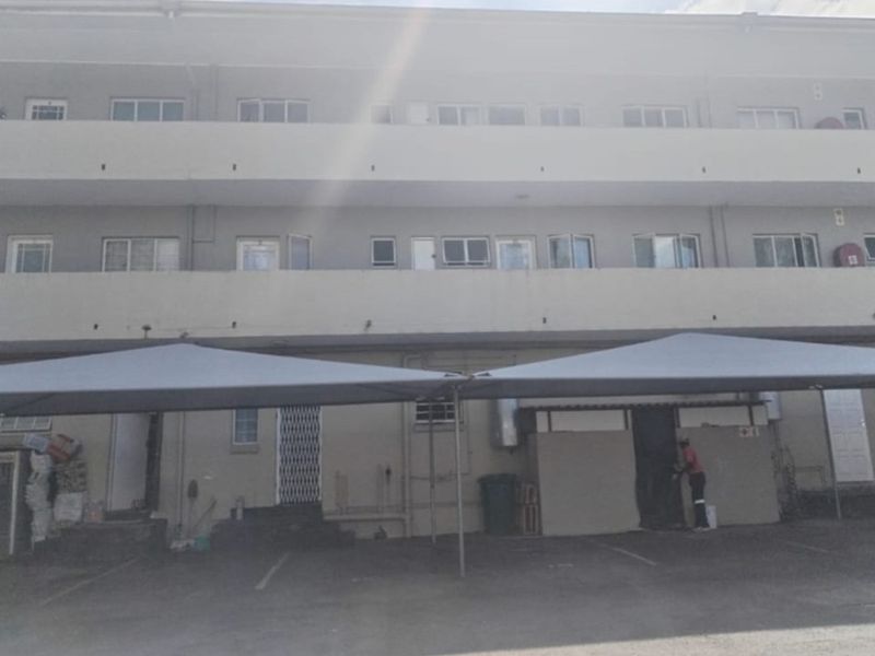 Front elevation of a multi-story apartment building featuring covered parking bays and security gates at the ground level entrance.