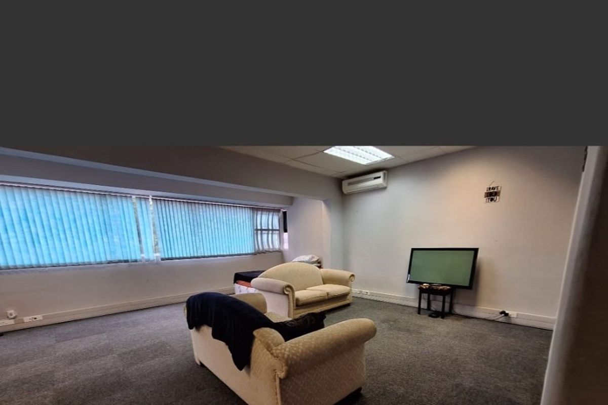 A living room featuring carpet flooring, vertical blinds, and a wall-mounted split-system air conditioner.