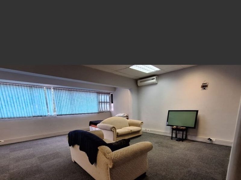 A living room featuring carpet flooring, vertical blinds, and a wall-mounted split-system air conditioner.