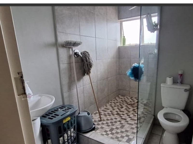 A functional bathroom featuring a tiled shower enclosure with a glass screen, a pedestal basin, and a standard toilet.