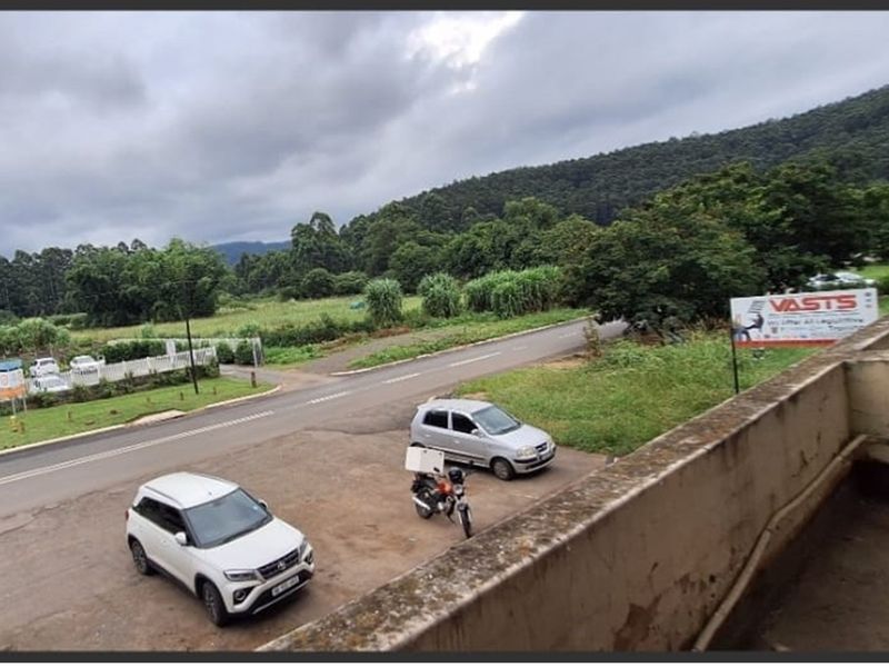 Elevated view overlooking a road, surrounding greenery, and distant hills, captured from a balcony with a weathered concrete railing.