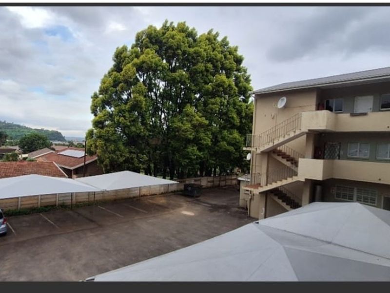 View of the apartment complex rear exterior, featuring paved parking area with shade cloth carports and an external staircase providing access to upper levels.