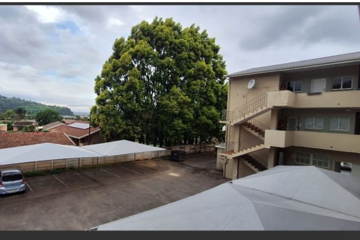 View of the apartment complex rear exterior, featuring paved parking area with shade cloth carports and an external staircase providing access to upper levels.