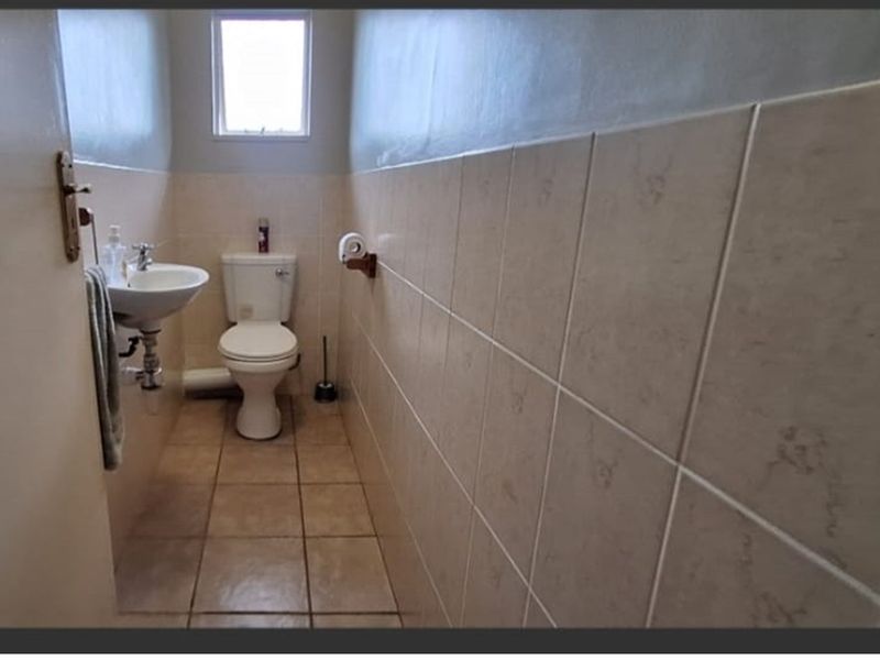 A compact bathroom featuring a wall-mounted basin, toilet, and neutral ceramic wall and floor tiling.