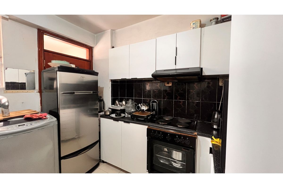 Compact kitchen featuring white cabinetry, black tiled backsplash, built-in oven, and extractor fan, providing a functional workspace.