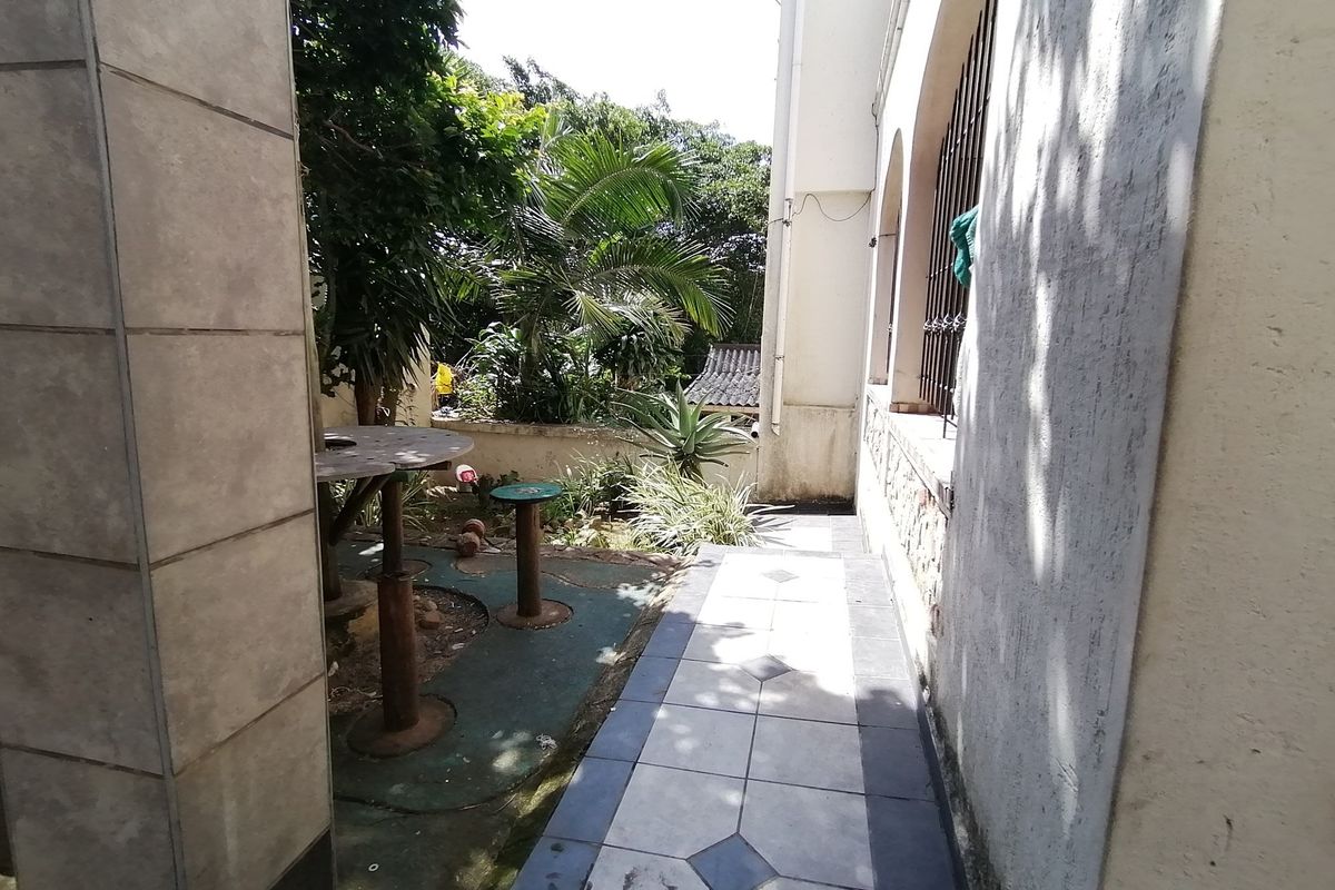 A side exterior walkway featuring tiled flooring and access to a small garden area with established greenery.