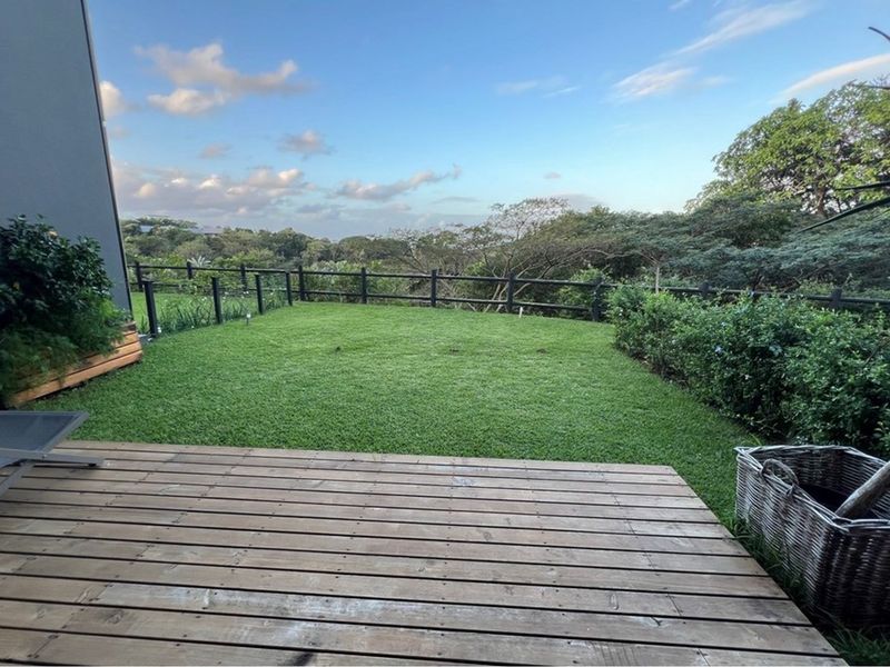 A well-maintained rear garden featuring timber decking, a manicured lawn, and a post and rail fence overlooking natural greenery.