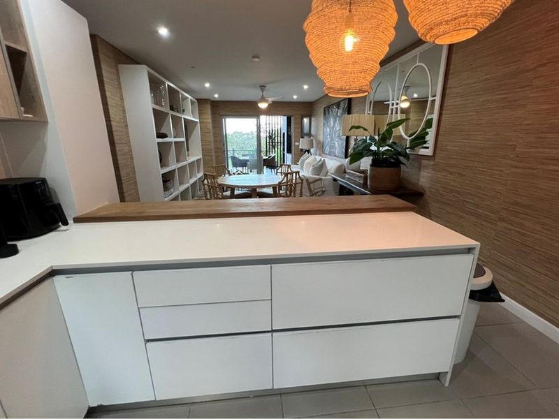 Modern open-plan living area featuring a sleek kitchen island with stone countertops, integrated cabinetry, and seamless flow to the dining and balcony spaces.