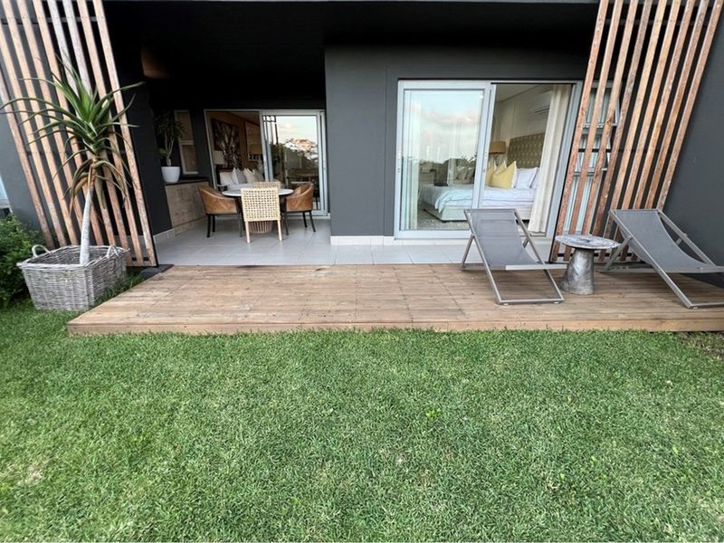 A modern ground-floor patio featuring timber decking, tiled flooring, and sliding glass doors that provide seamless access to the interior living and bedroom spaces.