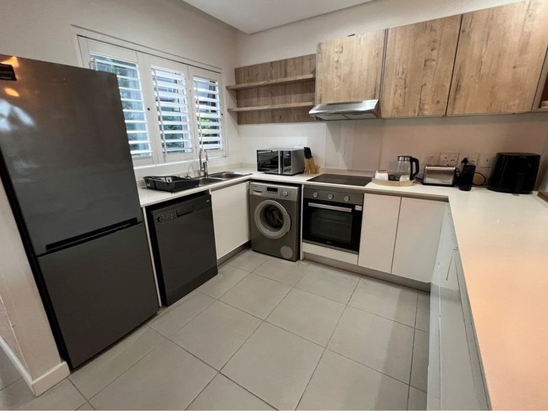 Modern kitchen featuring sleek white and wood-tone cabinetry, stone countertops, integrated appliances, and tiled flooring with functional shutter blinds.