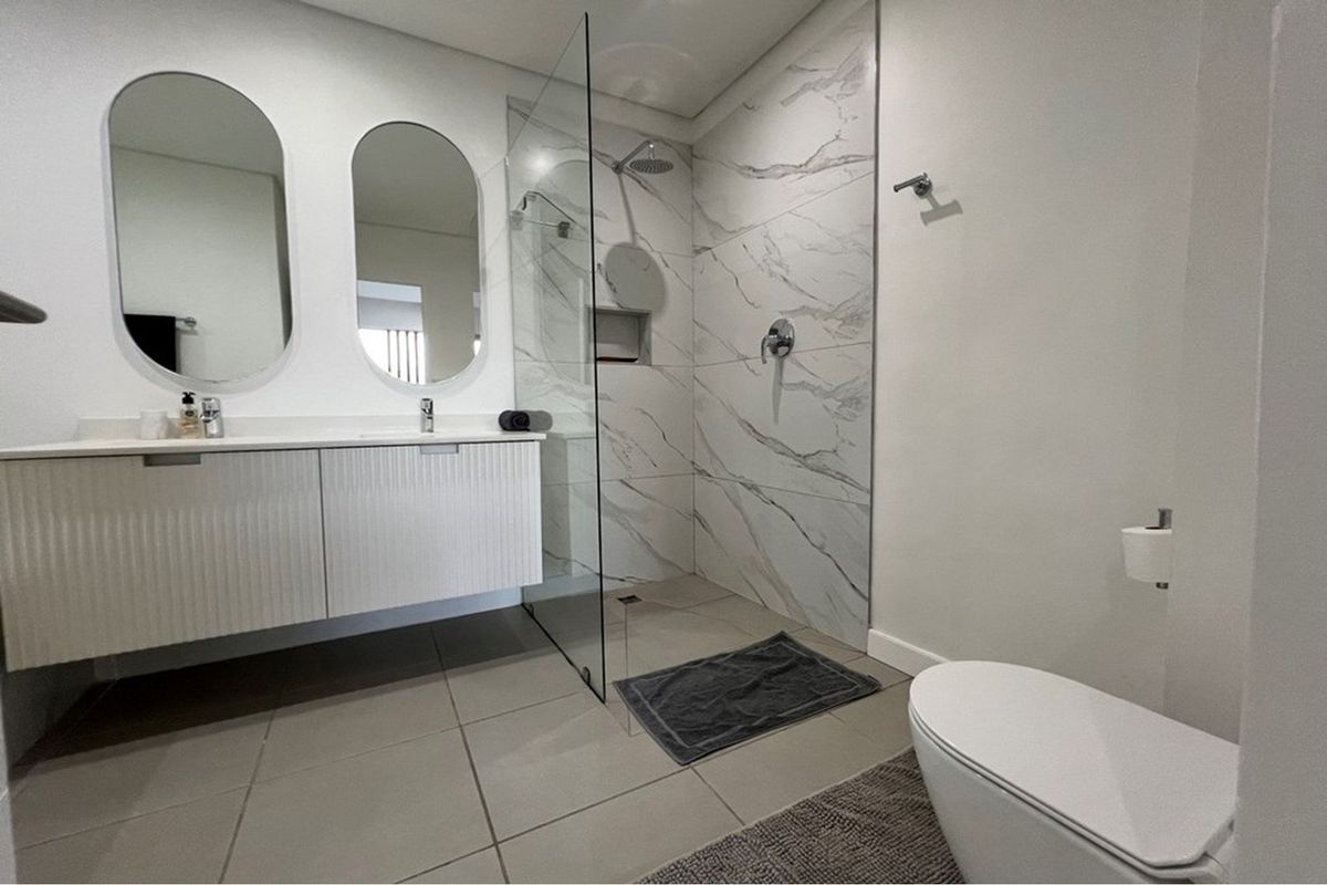 Modern bathroom featuring a double vanity with wall-mounted cabinetry, a spacious walk-in shower with marble-look tiling, and high-quality fixtures.