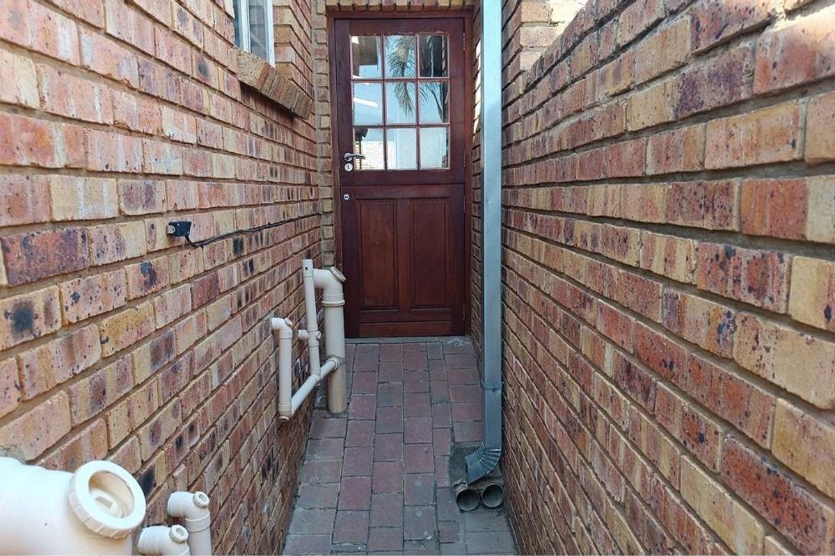 A narrow side passage featuring brick paving, exposed exterior plumbing, and a wooden door providing access to the property.