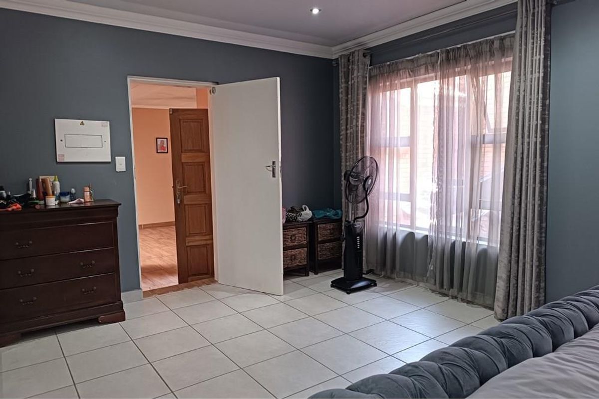 A bedroom featuring tiled flooring, dark grey walls, and a large window with curtains, providing access to an adjacent room.