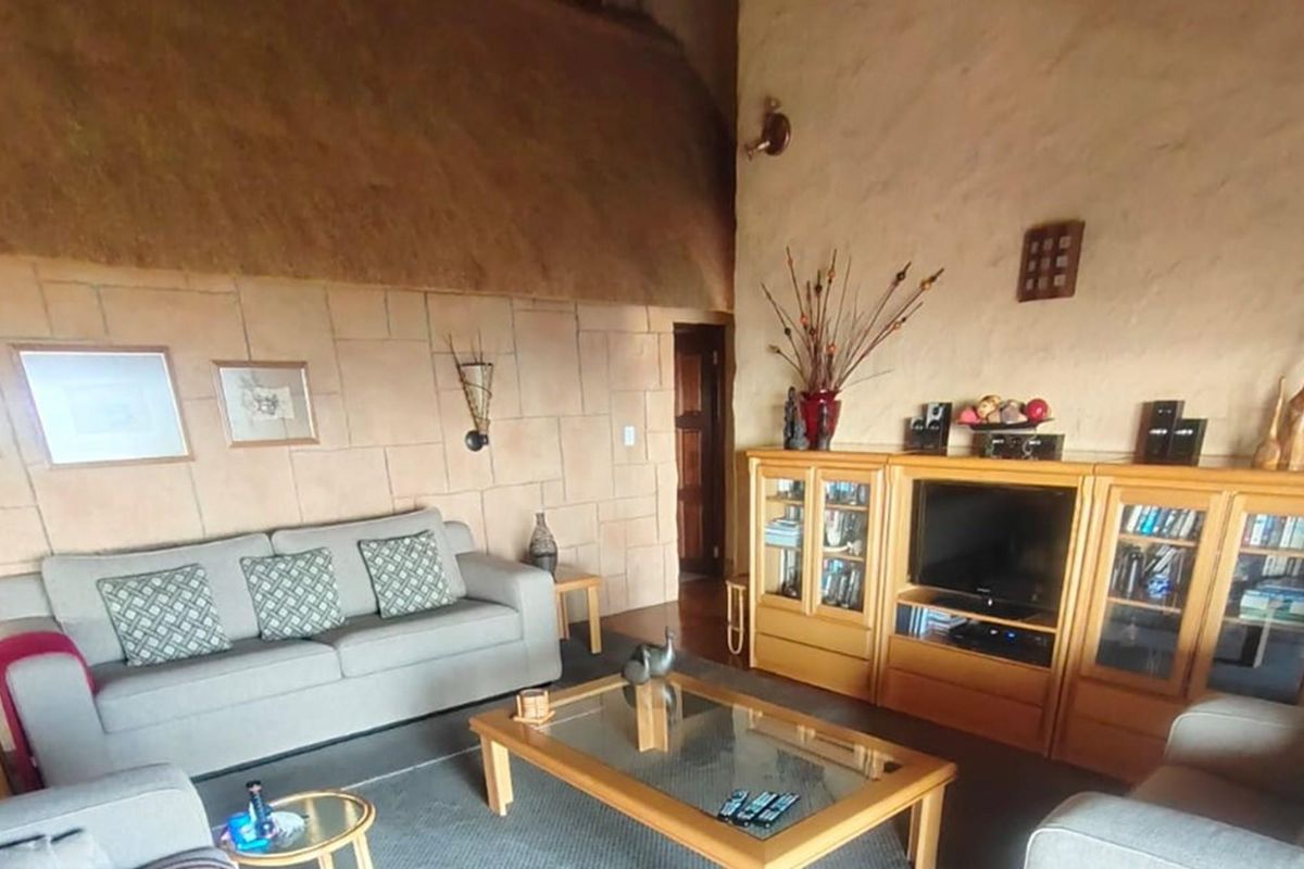 A cozy living room featuring textured stone-clad walls, a high vaulted thatched ceiling, and warm ambient lighting.