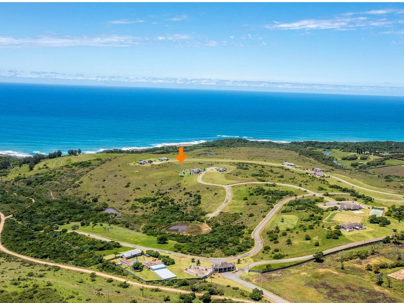 An aerial view of a coastal residential estate featuring rolling hills, established road infrastructure, and proximity to the ocean.