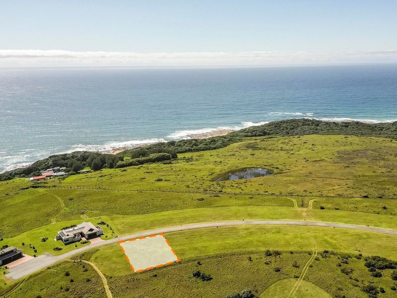 Aerial view of a vacant residential plot situated in a coastal estate, featuring road access and scenic ocean views.