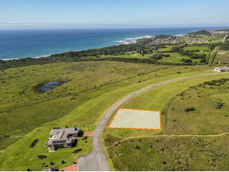 An aerial view of a vacant residential land plot situated in a coastal estate, featuring road access and scenic ocean views.