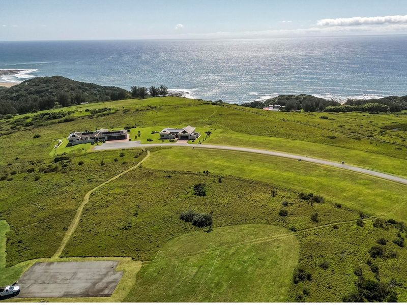 An aerial view of a large residential property situated on a grassy coastal landscape with ocean views and paved access roads.