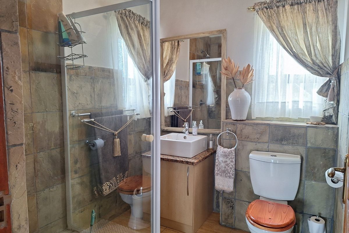 A functional bathroom featuring a glass shower enclosure, vessel sink with granite vanity, and neutral ceramic tiling throughout.