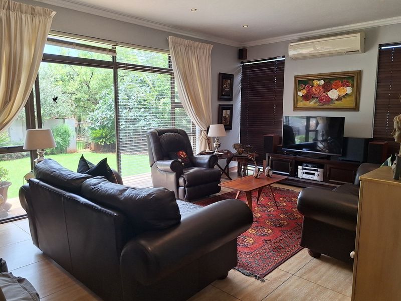 A comfortable living room featuring tiled flooring, recessed downlighting, a wall-mounted air conditioning unit, and large sliding glass doors providing access to the garden.