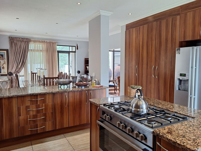 Spacious open-plan kitchen featuring wood veneer cabinetry, granite countertops, and a gas hob, seamlessly flowing into the adjacent dining area.