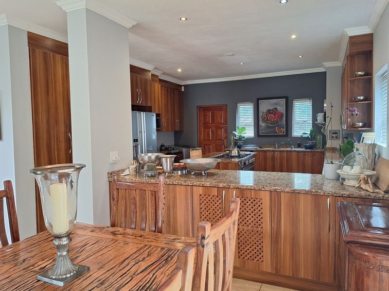 Open-plan kitchen featuring warm wooden cabinetry, granite countertops, and a gas hob, seamlessly flowing into the dining area with recessed lighting throughout.