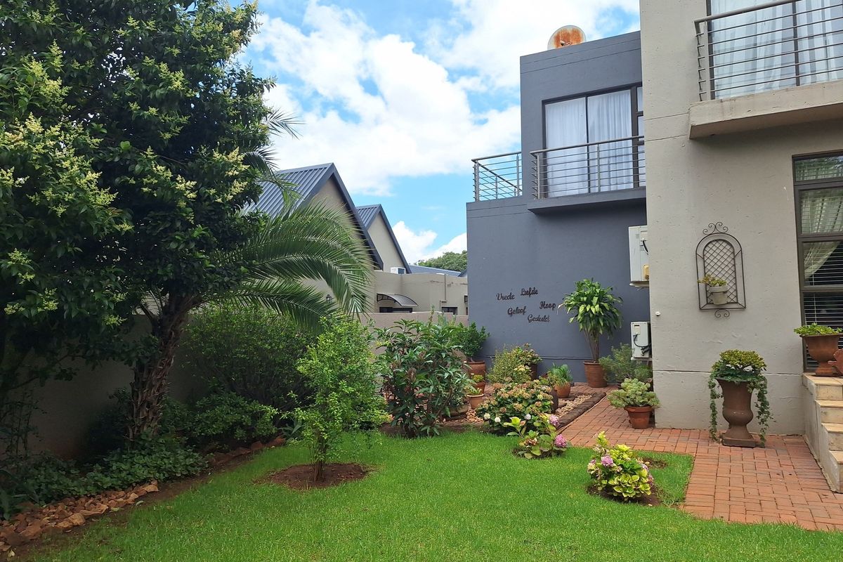 A well-maintained rear garden featuring brick paving, lush landscaping, and a modern two-story building facade with a private balcony.
