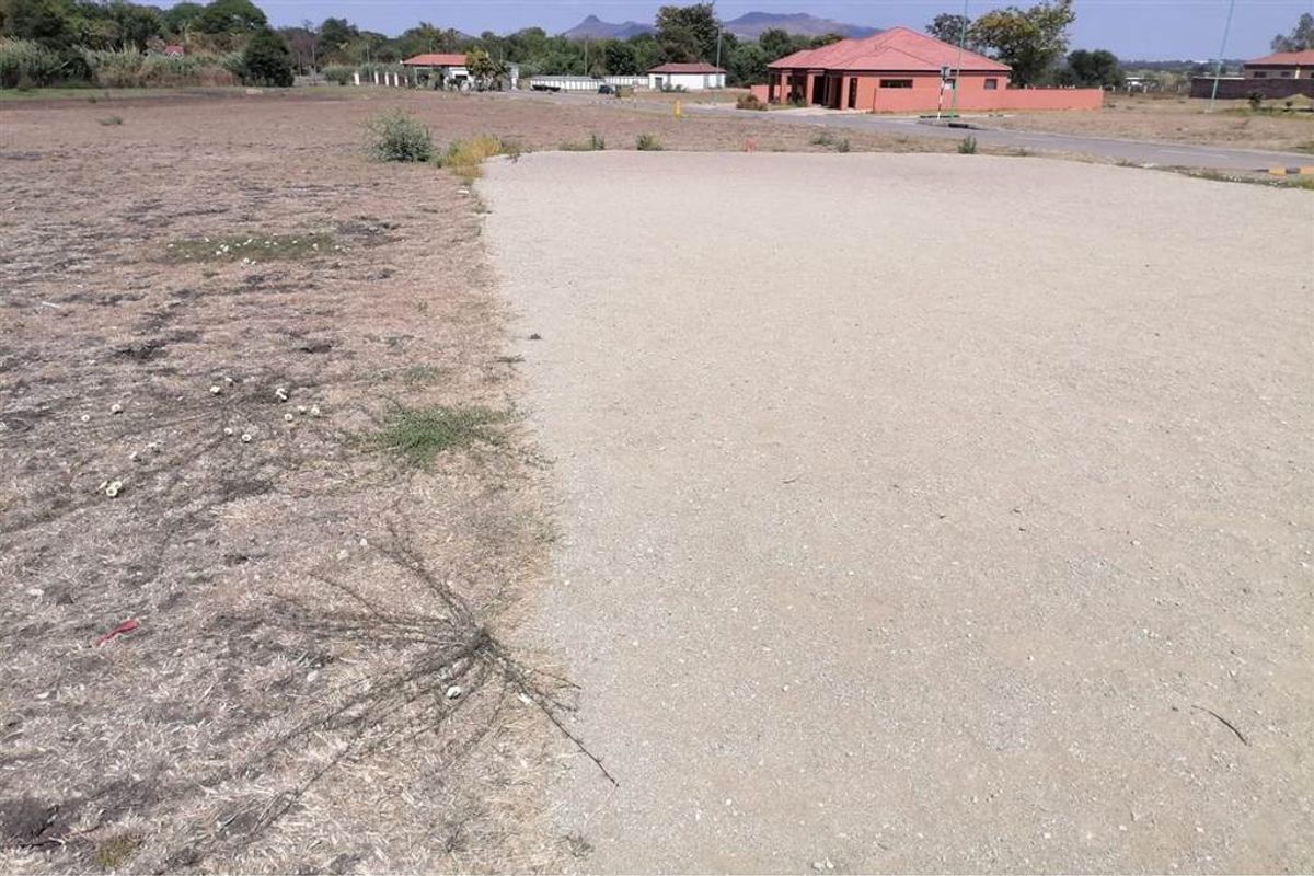 A view of a vacant residential plot featuring cleared land and a gravel surface, situated in a developed neighborhood.