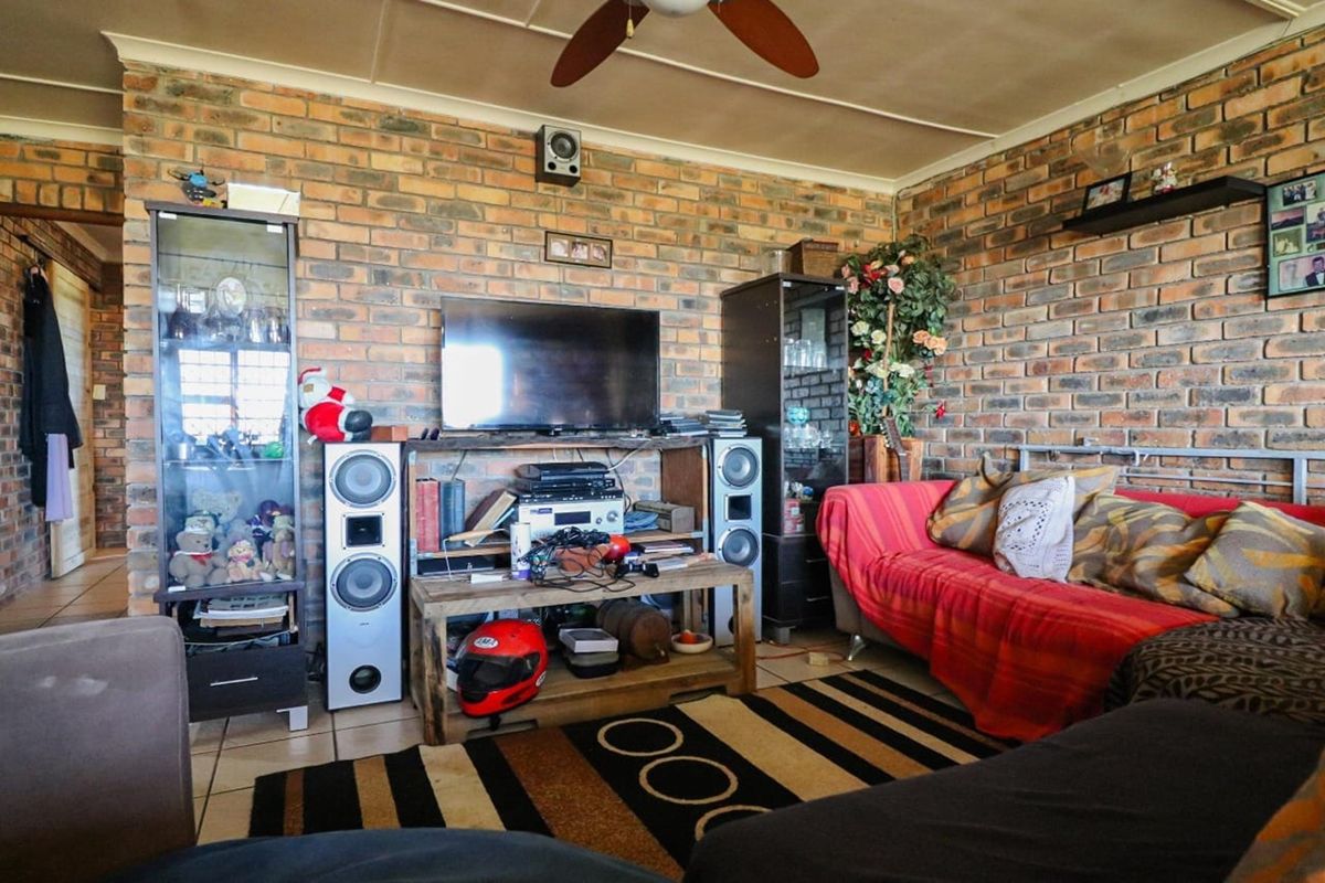 A rustic living room featuring exposed face-brick walls, tiled flooring, and a ceiling fan, offering a warm and character-filled space.