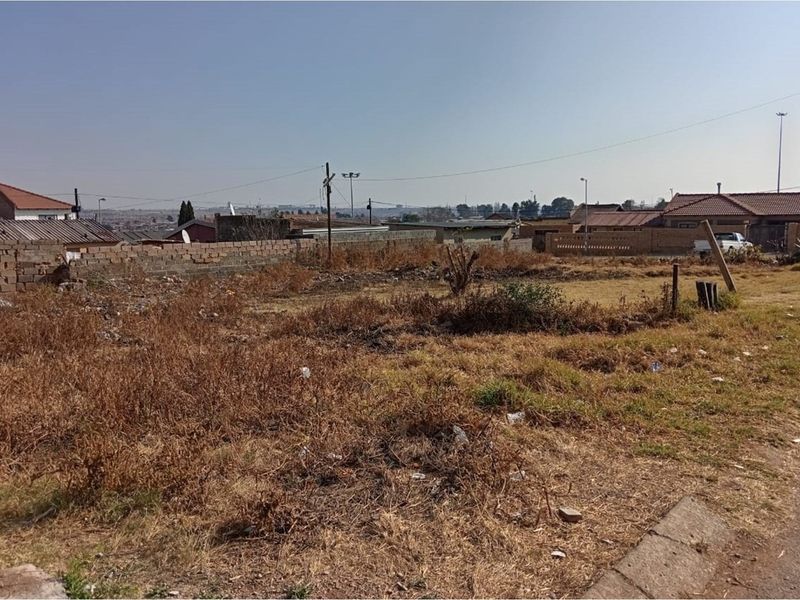 A vacant residential plot featuring a boundary wall and street-side kerb, situated in an established neighborhood.