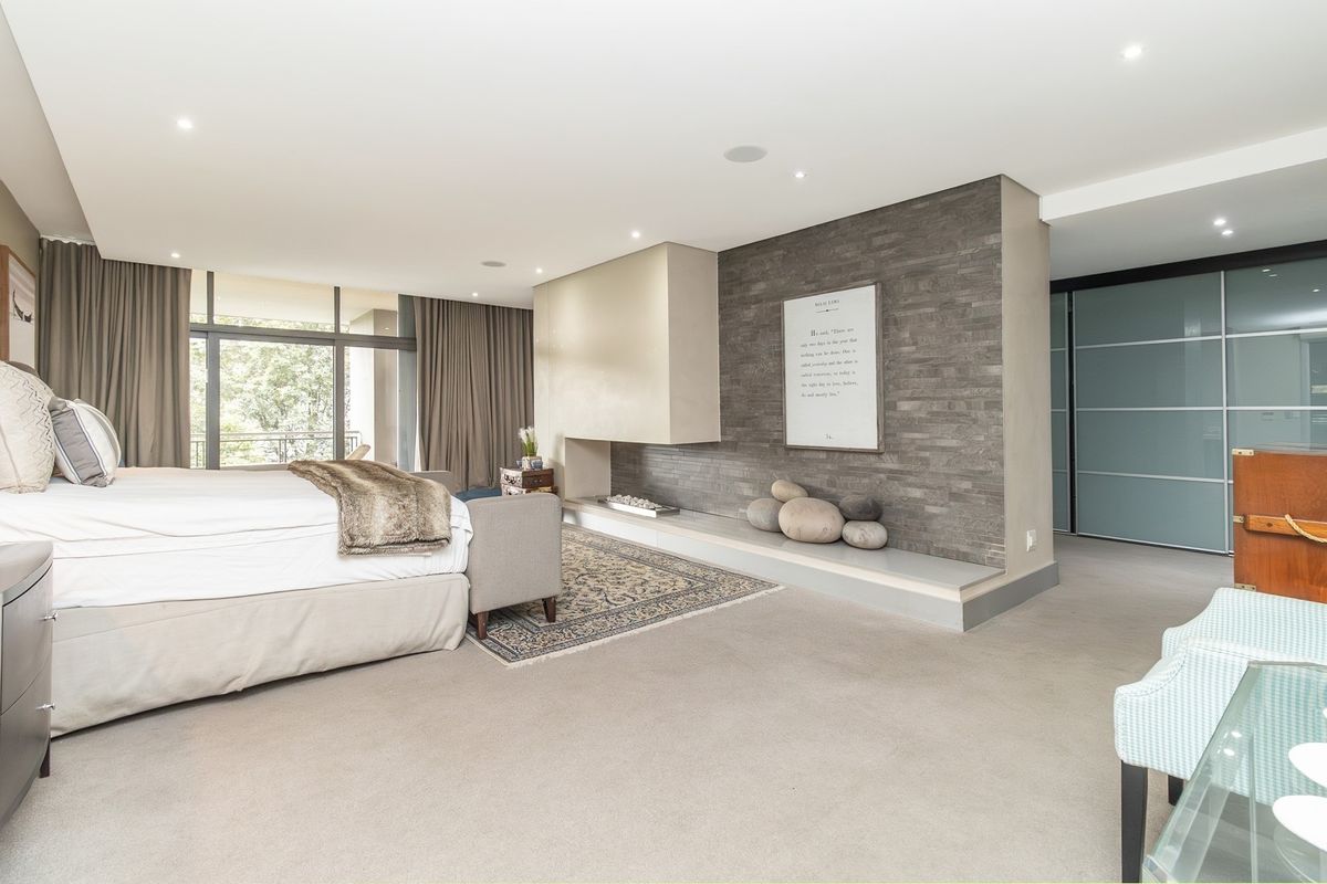 Spacious bedroom featuring a modern stone-clad feature wall with a built-in fireplace, recessed lighting, and large sliding glass doors leading to a balcony.