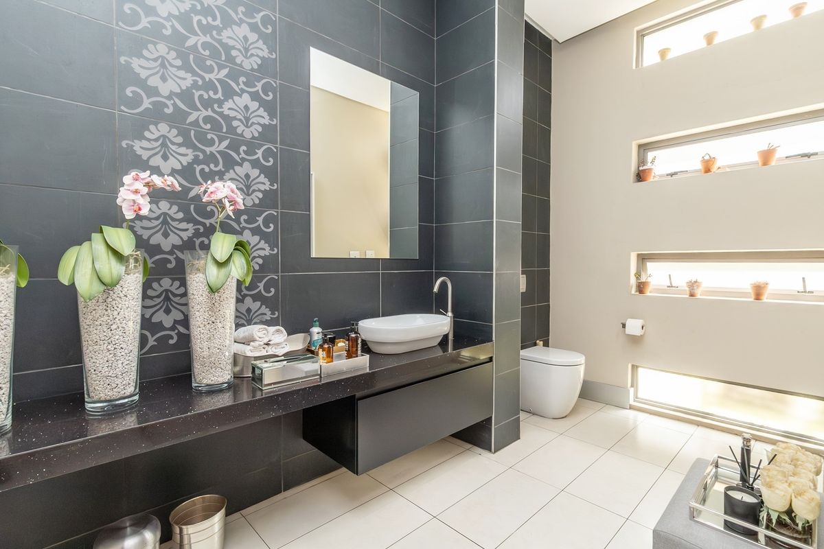 Modern bathroom featuring a floating vanity with a vessel sink, dark decorative wall tiling, and stacked horizontal windows providing natural light.