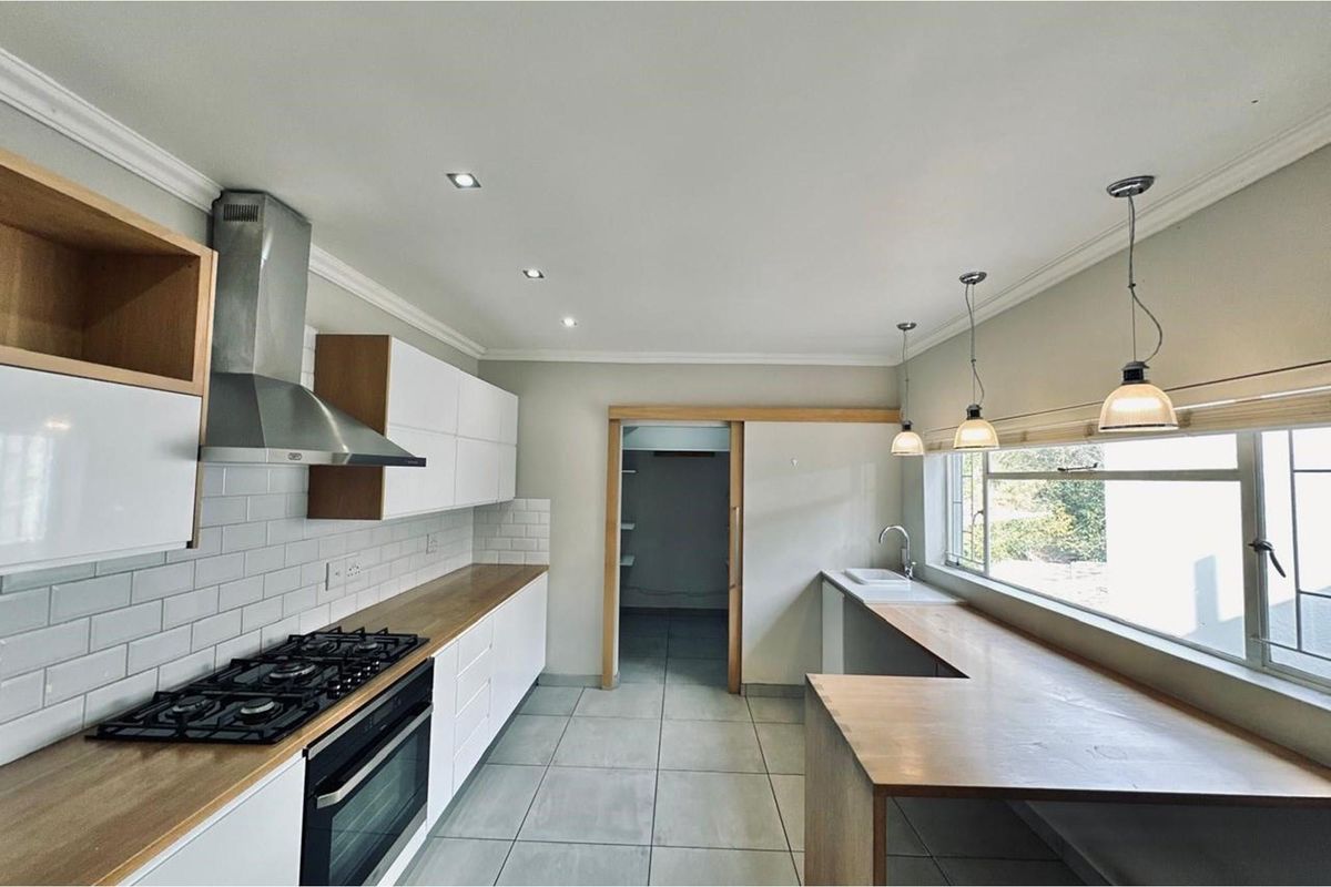 Modern kitchen featuring white cabinetry, wooden countertops, subway tile backsplash, built-in gas hob, oven, extractor fan, and a breakfast bar overlooking the garden.