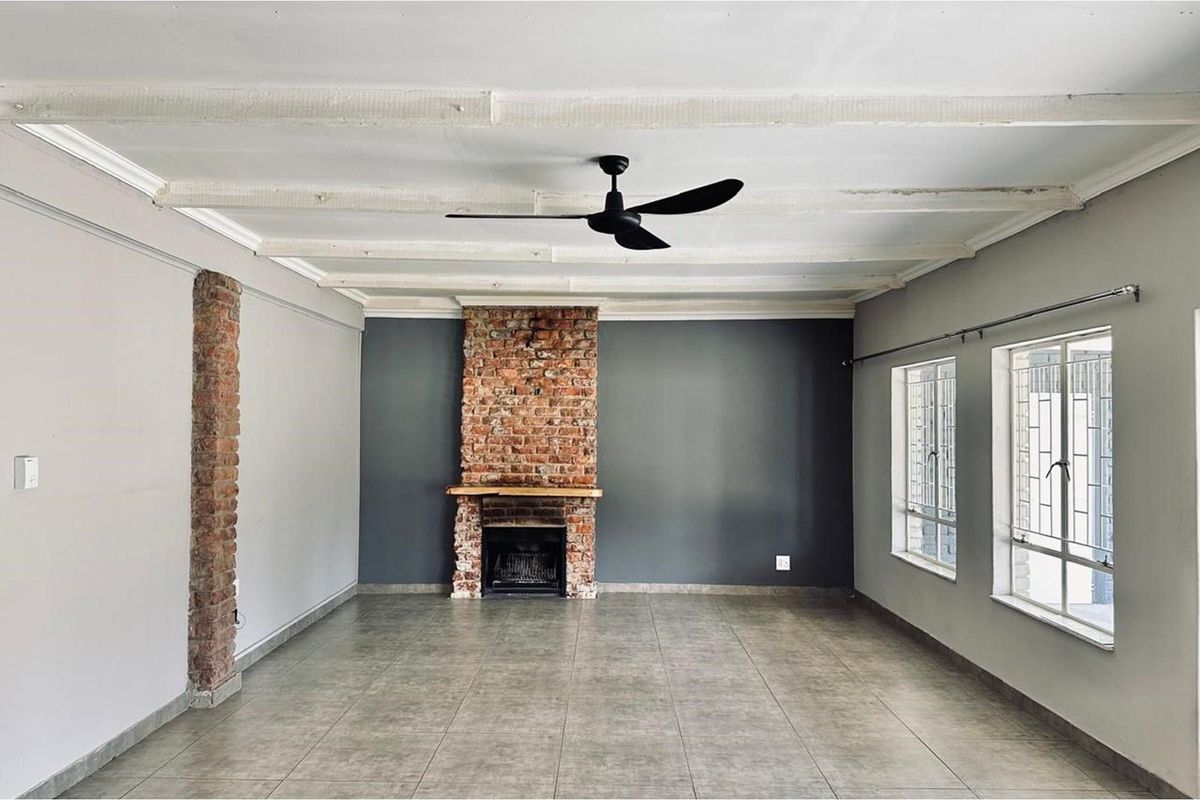Spacious living room featuring a prominent exposed brick fireplace, tiled flooring, and a ceiling fan, offering a clean and neutral canvas.