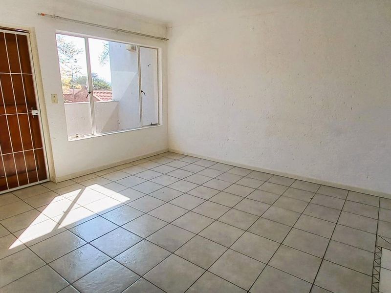 An empty living area featuring tiled flooring, a security gate, and an intercom system, offering a blank canvas for renovation.