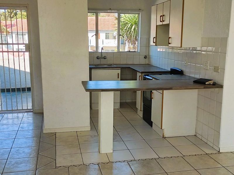 Open plan kitchen area featuring tiled flooring, built-in cabinetry, a breakfast bar, and direct access to an exterior balcony through a security gate.