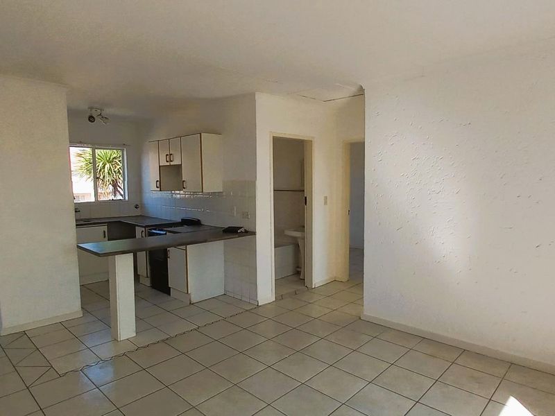 Open-plan living area featuring tiled flooring, a functional kitchen with built-in cabinetry, and a breakfast bar, leading to an exterior security gate.