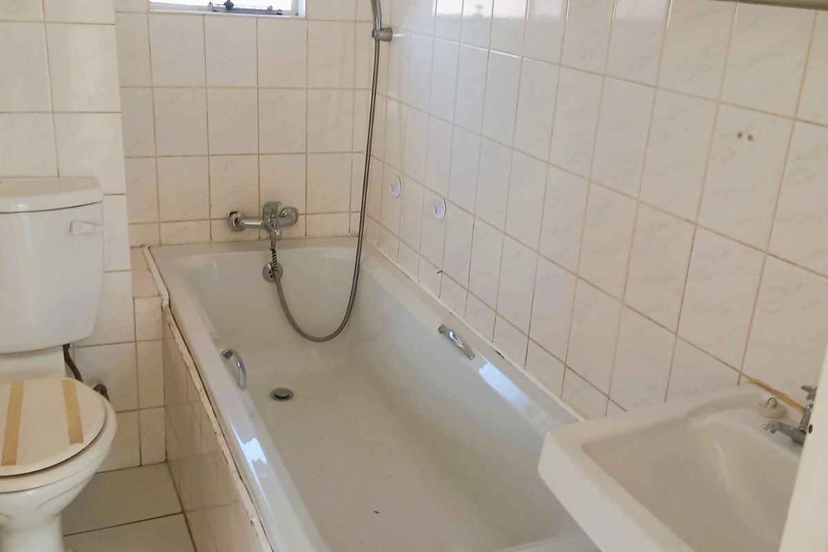 A dated bathroom featuring a standard bathtub, toilet, and wall-mounted basin with tiled walls, requiring cosmetic updates to improve its overall condition.