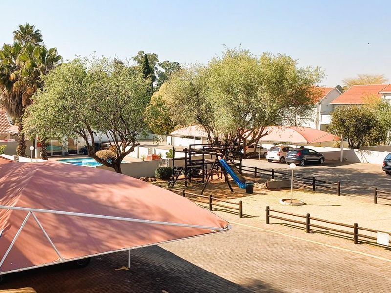 An elevated view of the townhouse complex grounds, featuring paved parking areas with shade cloth carports, a children's play area, and a swimming pool.